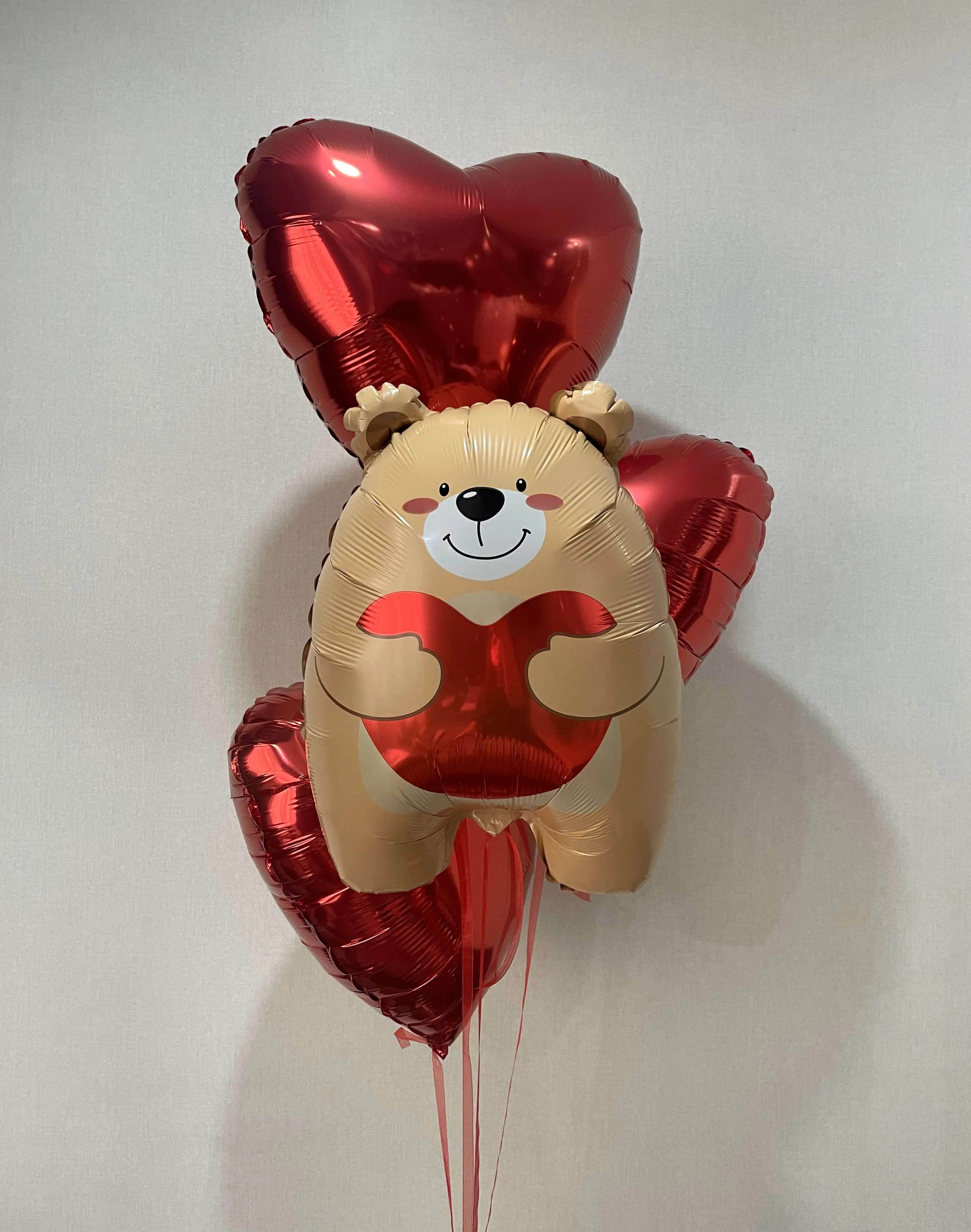 Композиция из фольгированных шаров: центральный элемент — мишка бежевого цвета с сердцем, окружённый тремя красными шарами-сердцами
